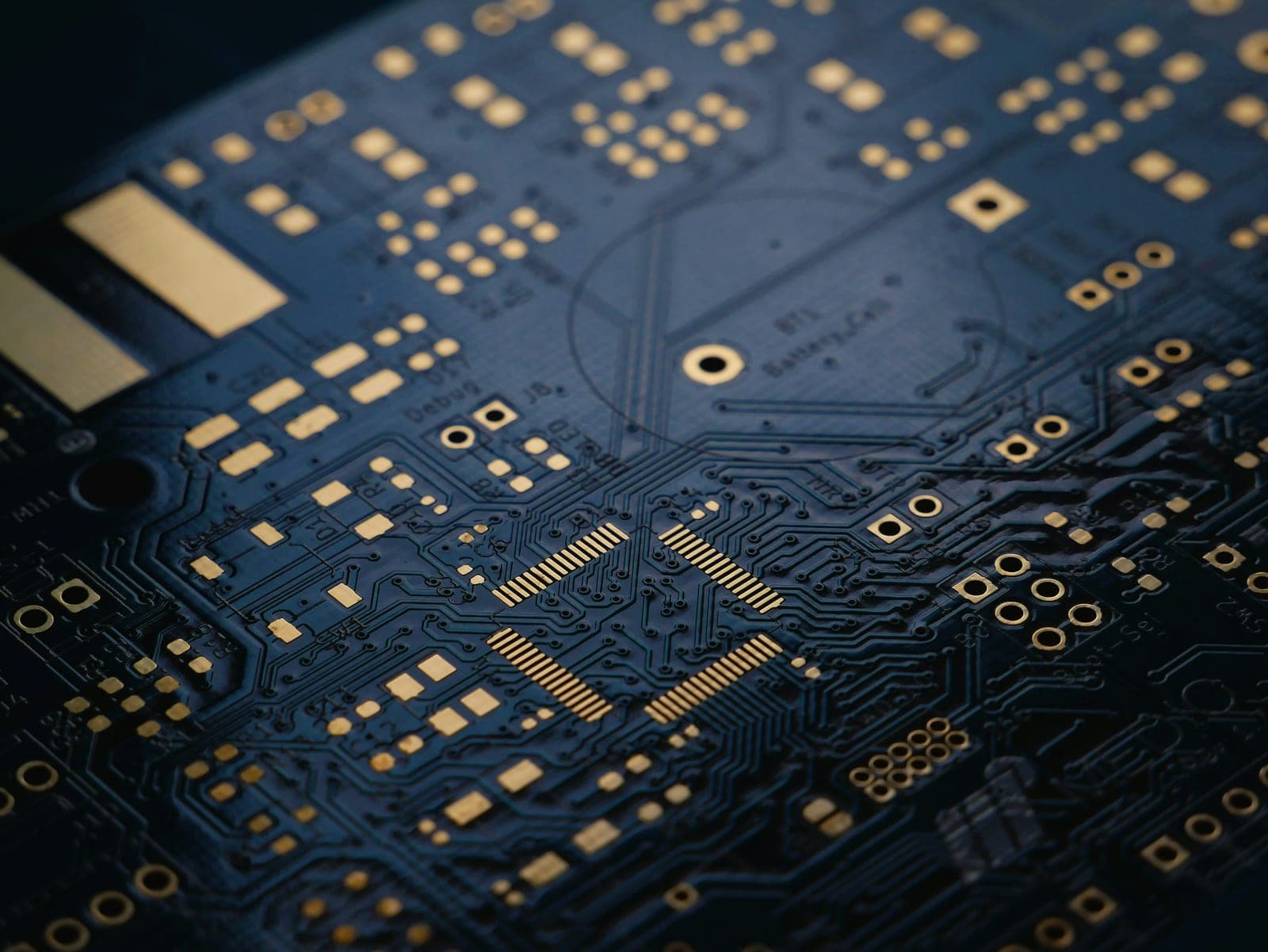 Macro of a dark blue printed circuit board with gold contact pads and fine copper traces
