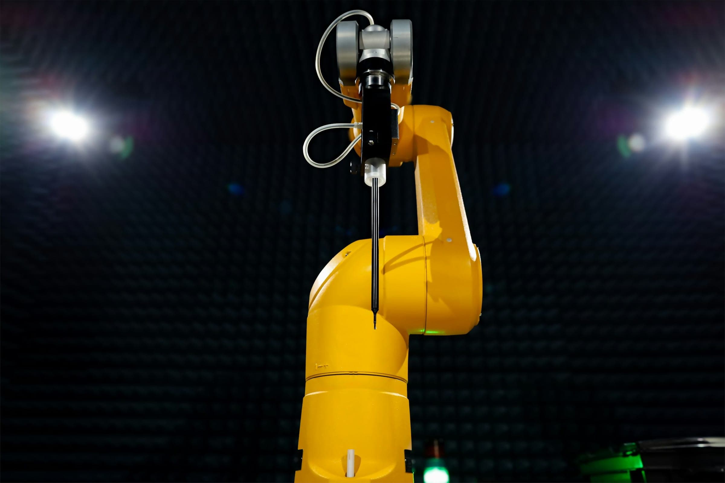Yellow industrial robotic arm in a dark anechoic chamber lined with foam absorbers