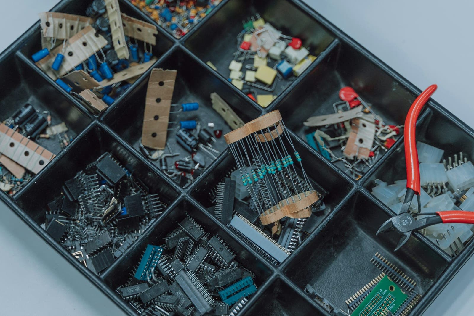Compartment tray of electronic components — resistors, chips and connectors — with red-handled pliers