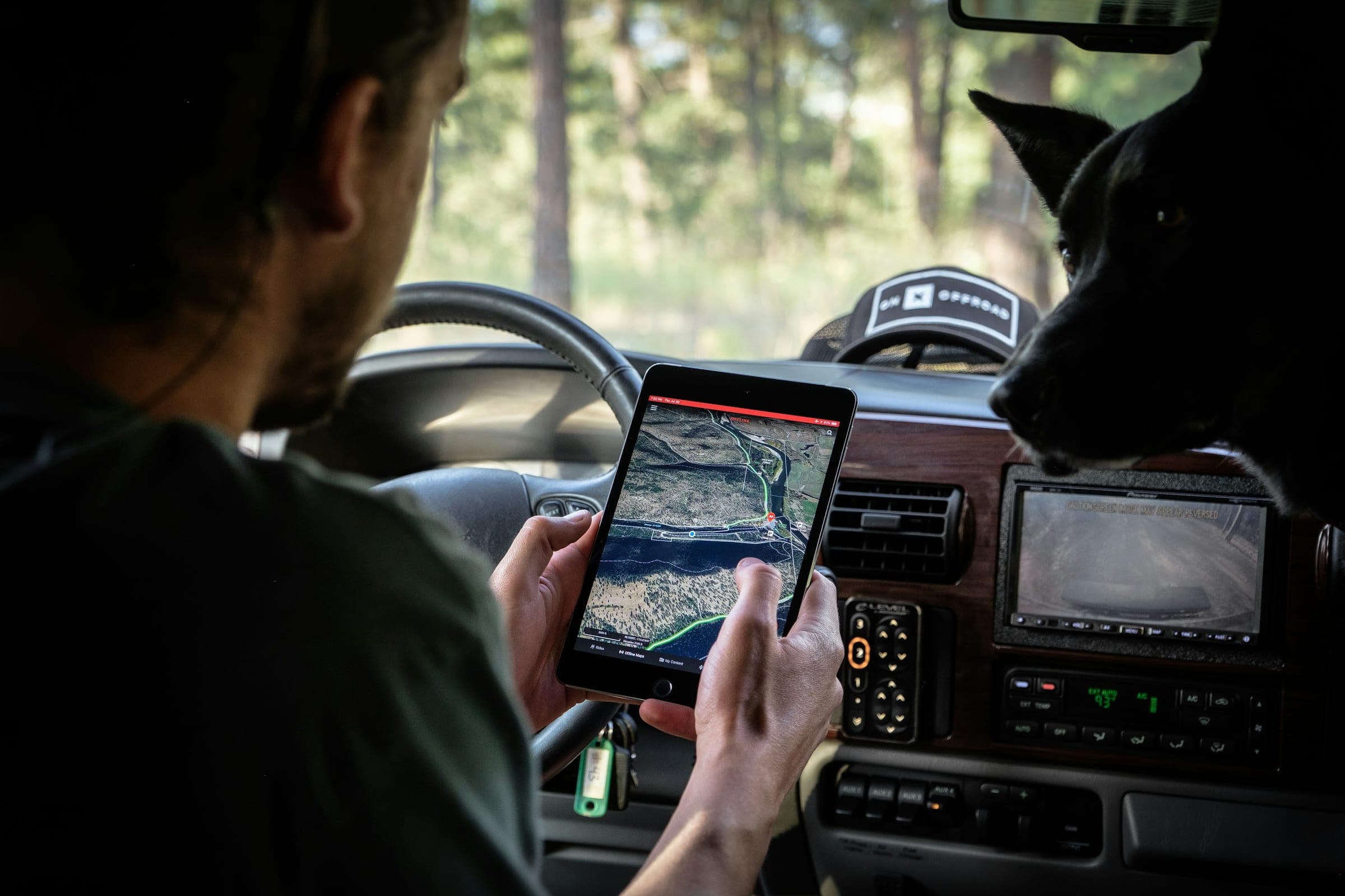 Driver in a vehicle cab studying a terrain map on a tablet, seen over the shoulder